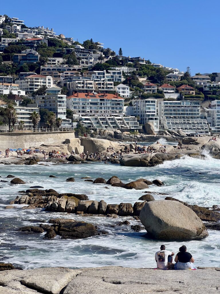 Cape Town, Sea Point on a sunny day, people sunbathing on the sand by the ocean with seals sunbathing on the rocks in the ocean.